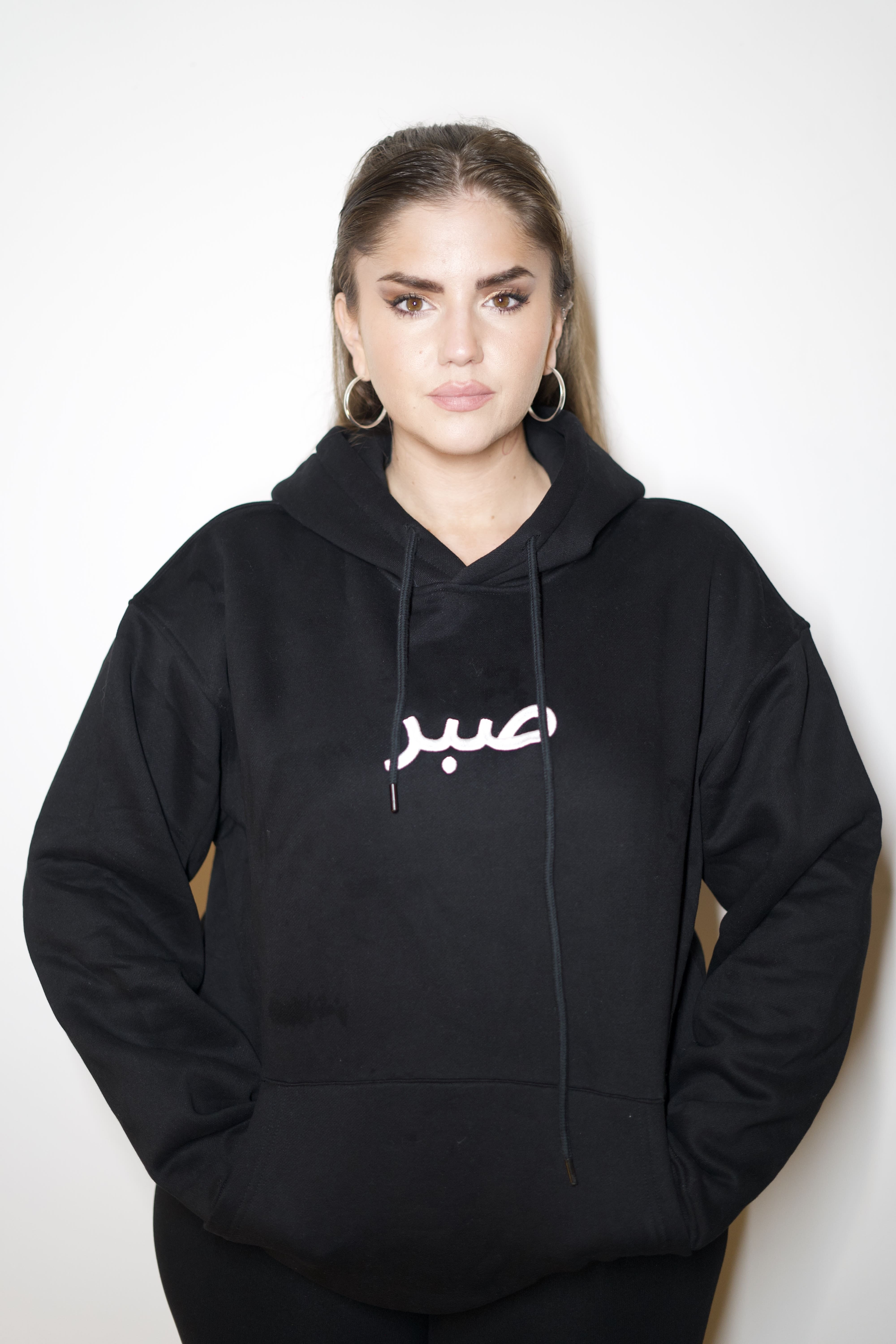 Femme portant un sweat à capuche noir avec broderie calligraphie arabe Sabr صبر - Talisma